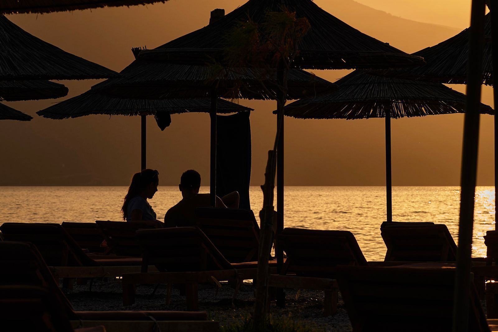 Una coppia sotto gli ombrelloni di paglia al tramonto sulla spiaggia di Valona