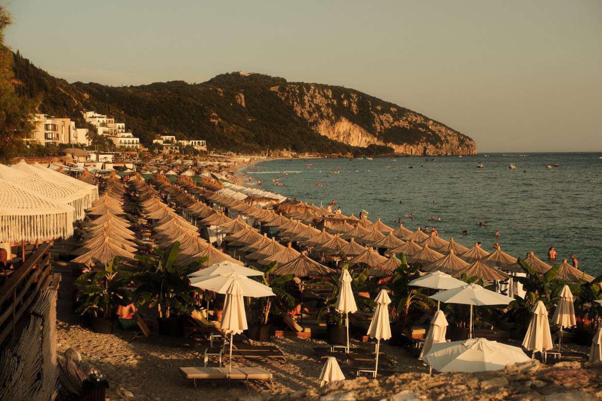 Spiaggia di Valona al tramonto con ombrelloni di paglia e bagnanti